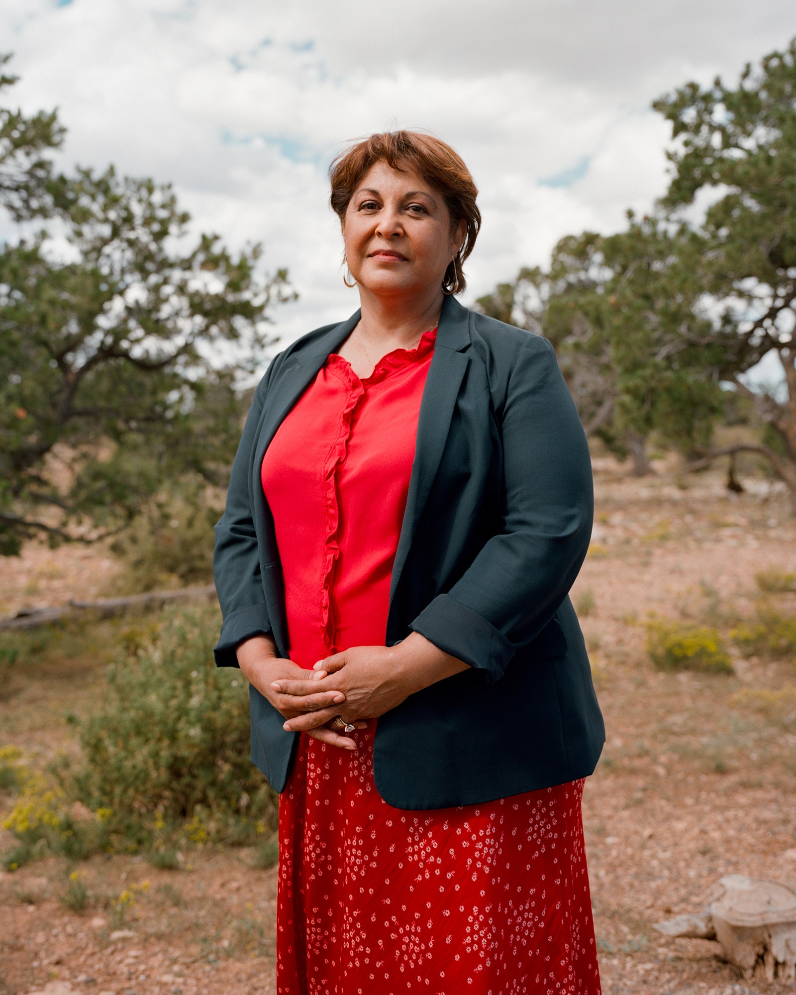 A person posing for a portrait outside. They wear a red patterned skirt red blouse and dark blue blazer.