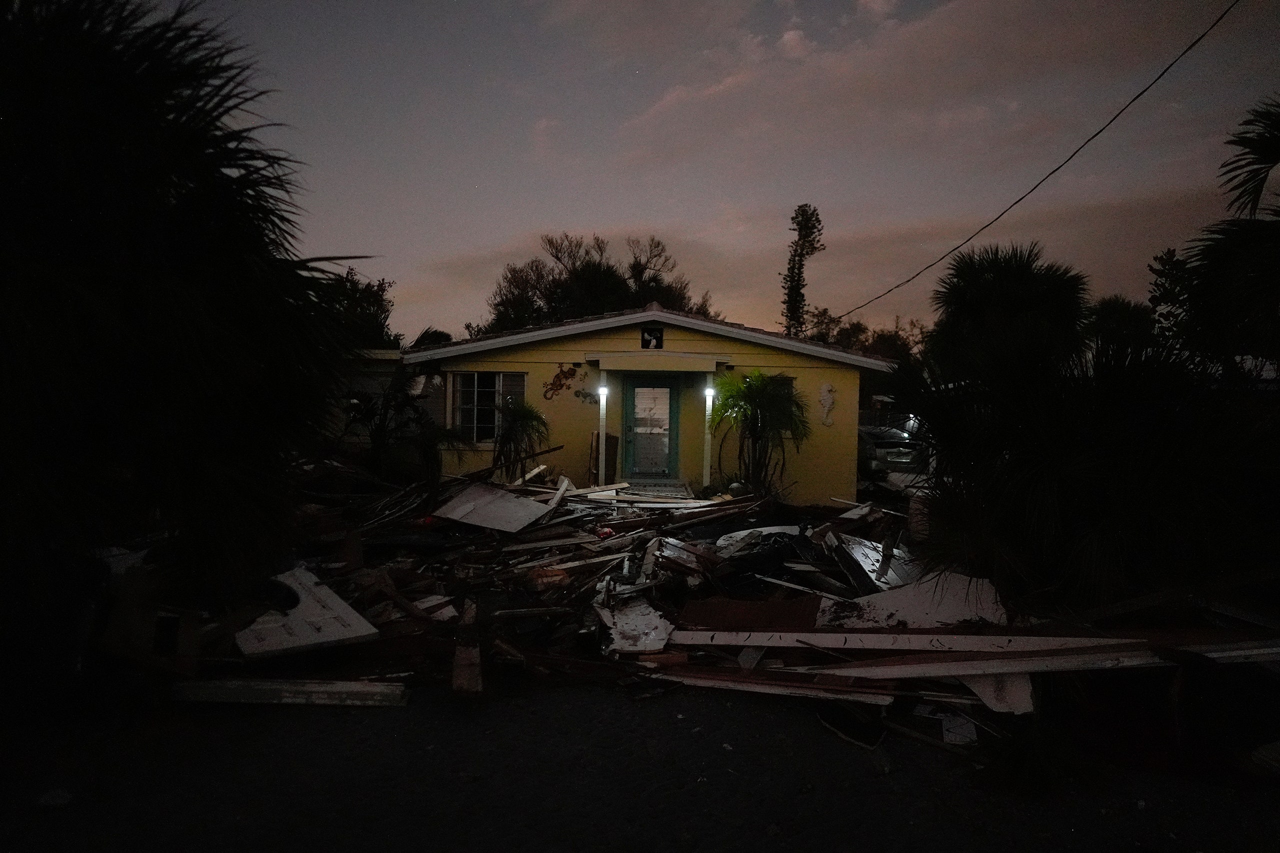 Outside lights that don't require electricity shine as night falls on a home surrounded by the debris of damaged...