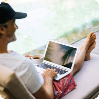 Man with a hat on in shorts by the pool looking at his laptop