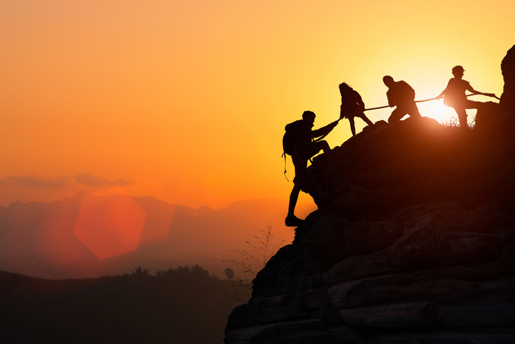 Silhouette of the climbing team helping each other while climbing up in a sunset. The concept of aid.