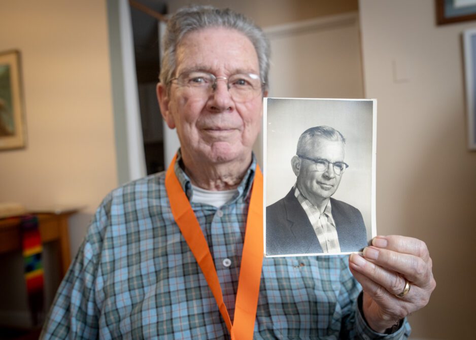 A senior gentleman holds a black and white photo of another man