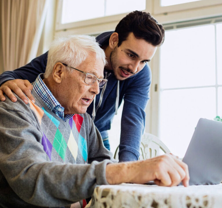 Adult son viewing a laptop computer screen with his elderly father