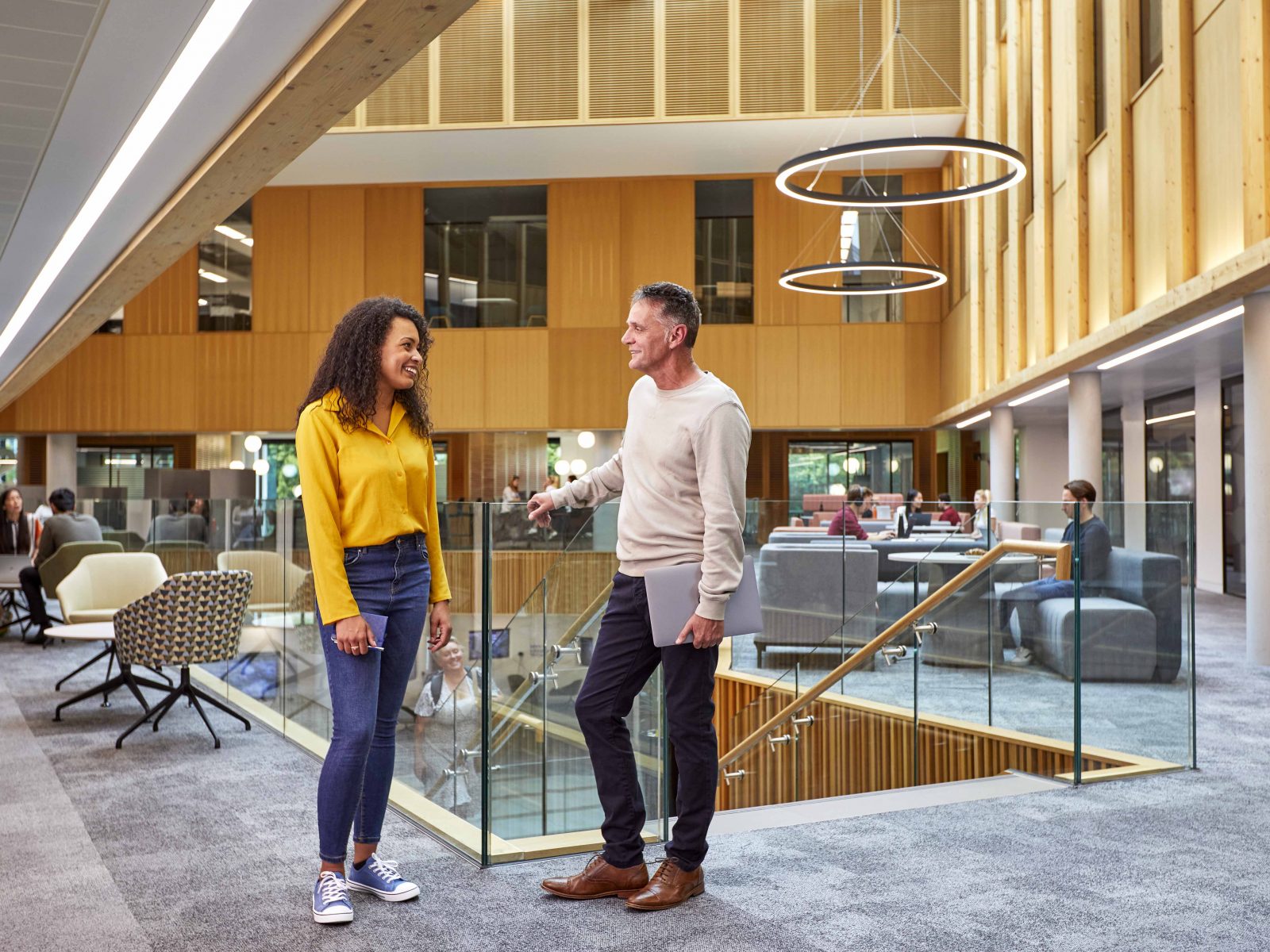 Two people having a conversation with people working behind them in the Nexus atrium