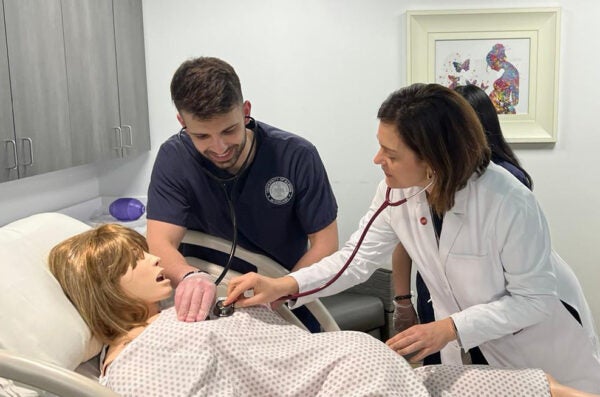 A student and a professor check the heartbeat of a high-fidelity manikin