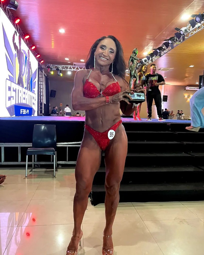 Claudia Oliveira in a red weightlifter bikini, holding her trophy.