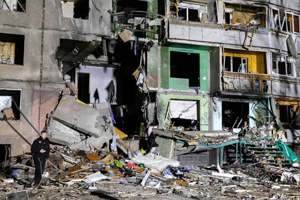 Side of an apartment building seen damaged by a Russian attack in Kharkiv, Ukraine, early on Friday, Nov. 8, windows and walls blasted out with piles of debris, burn marks, man walking through rubble.