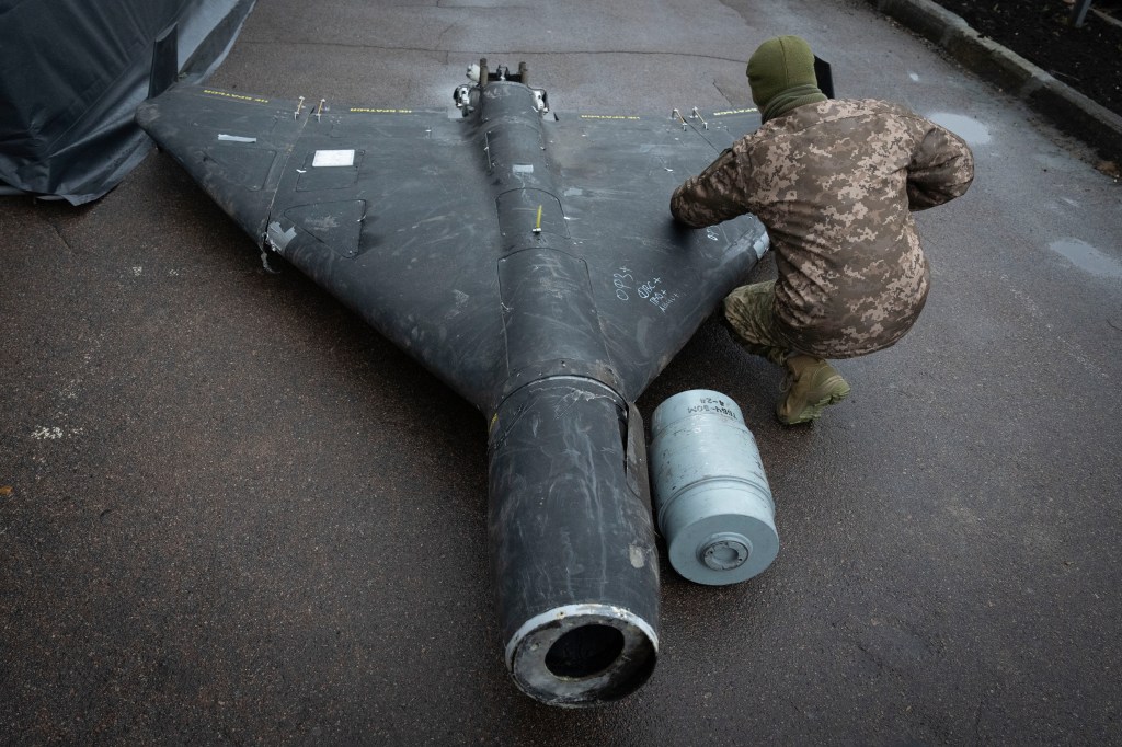 A Ukrainian officer examines a downed Shahed drone with thermobaric charge launched by Russia in a research laboratory in an undisclosed location in Ukraine, seen from behind with officer in camo and big black drone lying on floor