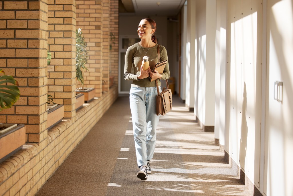 Happy female student walking alone in a university hallway, ready for learning and study