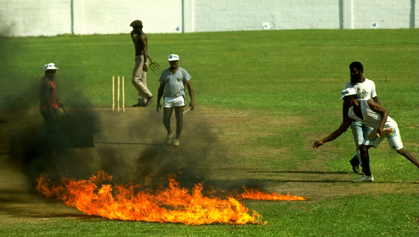 Ground staff set parts of the pitch alight to dry out damp areas before a tour match between Windward Islands and England