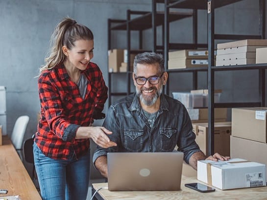 Unternehmerpaar sind in ihrem Lager vor dem Laptop und benutzen den GLS Partnerfinder