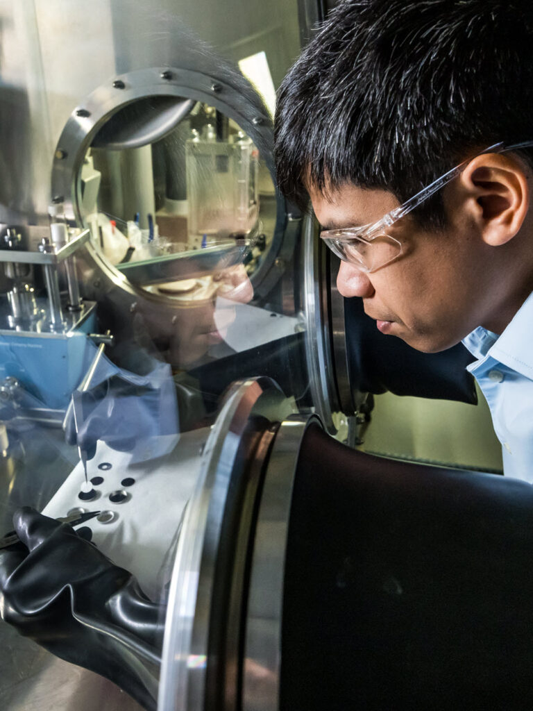 A male scientist assembles a coin cell by hand, using tweezers to drop in the synthesized solid electrolyte.