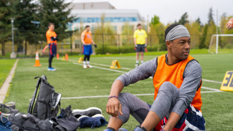 A photo of a man wearing athletic gear sitting on the sidelines of a football field