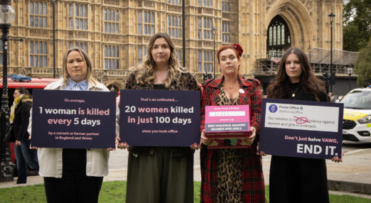 Four Refuge staff stand outside houses of parliament holding placards addressed to the prime minister.