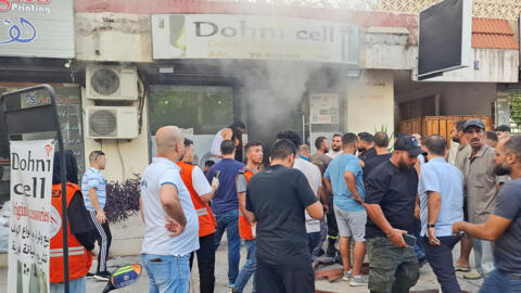 Residents gather as smoke rises from a mobile shop in Sidon, Lebanon, September 18, 2024.