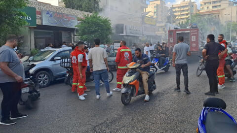 People gather as smoke rises from a mobile shop in Sidon, Lebanon, 18 September 2024. 