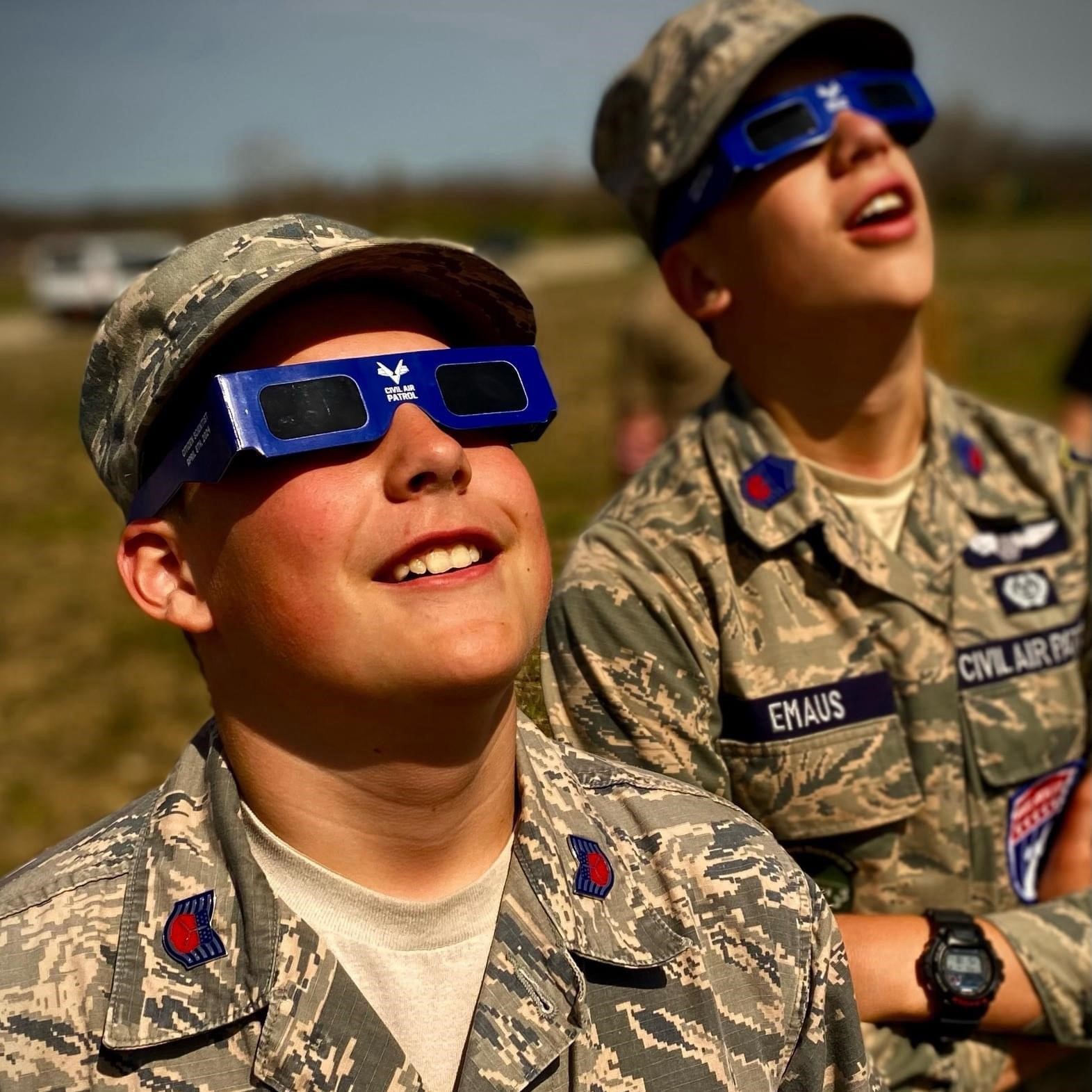 Two male cadets wearing solar viewing glasses stare with excitement into the distance.