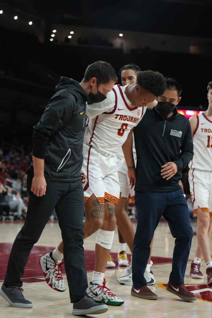 Dr. Alex Weber and Athletic Trainer Jon Yonamine assist basketball player Boogie Ellis