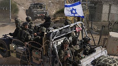 Israeli soldiers with the national flag stand on an armoured vehicle after crossing the security fence near the so-called Alpha Line that separates the Israeli-controlled Gola