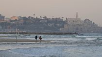 A couple walks along the shore of a beach in Tel Aviv, Israel.