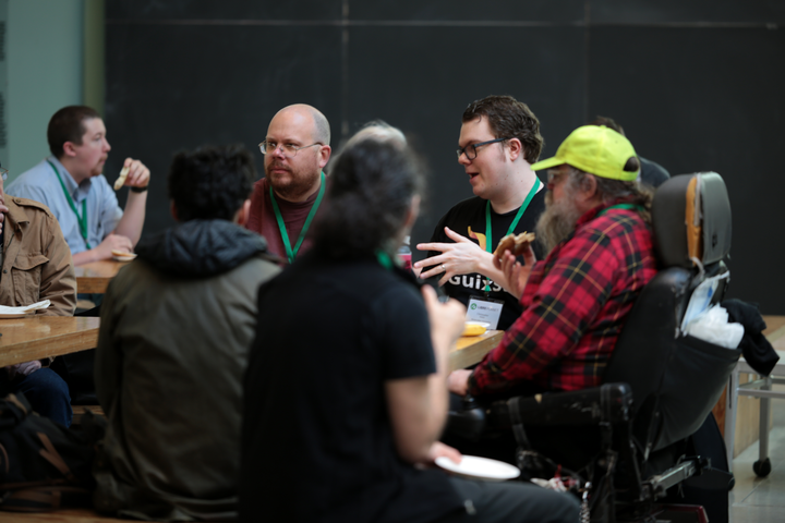 A group of hackers sitting around a table, talking with one another.