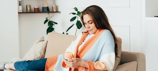 Junge Frau mit iPhone liegt auf Sofa.