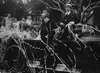 A black-and-white photograph of a group of people sitting on a 1920s style vehicle with party streamers draped across them and the car.