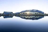 A view of a large canopy structure with a stormwater pond in the foreground.