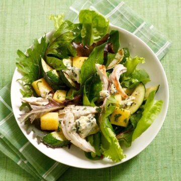 Close up of Warm Polenta Zucchini Salad in white bowl on green surface