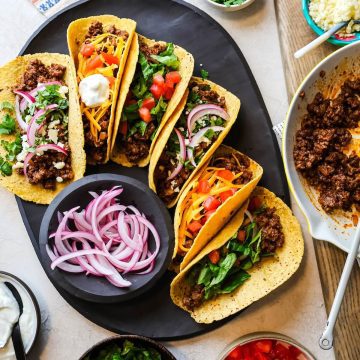 beef tacos on a serving platter with pickled red onions in a bowl.