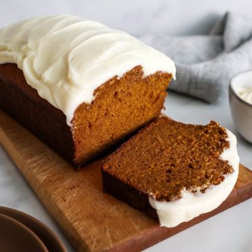 Feature image of pumpkin bread with cream cheese frosting, sliced on a cutting board.