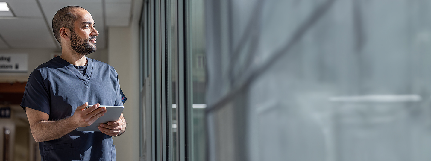 Employee holding a tablet while gazing through a window.