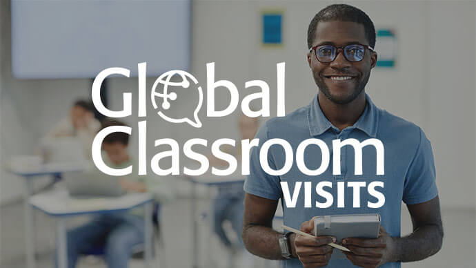 Global Classroom Visits - Male STEM teacher smiling for a photo with classroom in the background