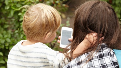 Hinterkopf von Frau und Kind, die beide auf ein Smartphone schauen