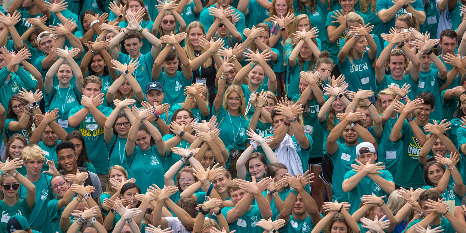 Students hold up their hands as wings while standing in bleachers