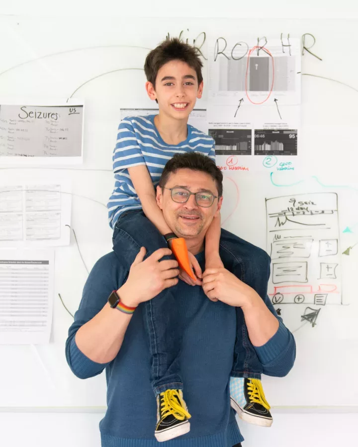 A man is holding his son in front of a whiteboard.