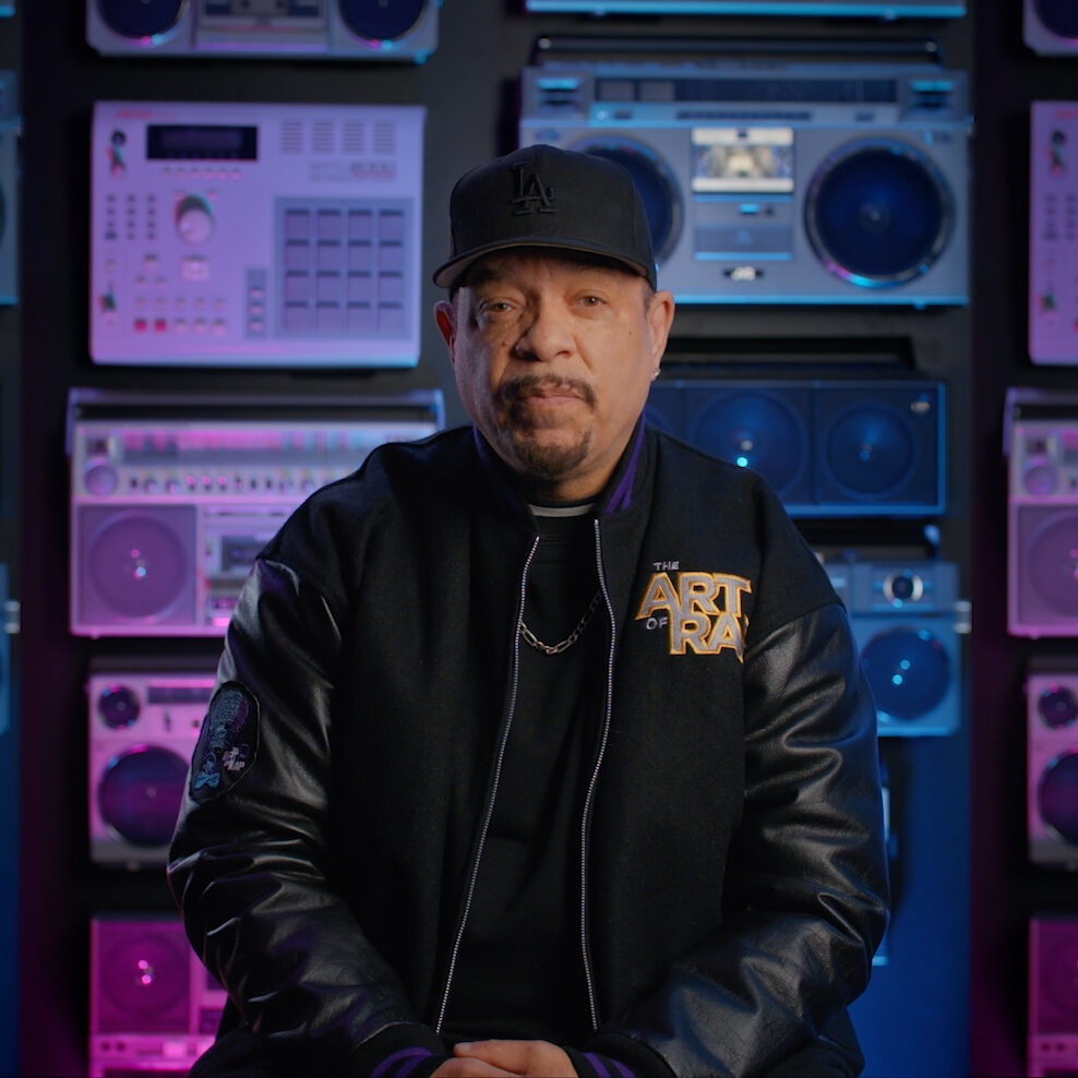 A man in a black jacket sitting in front of a set of stereos.