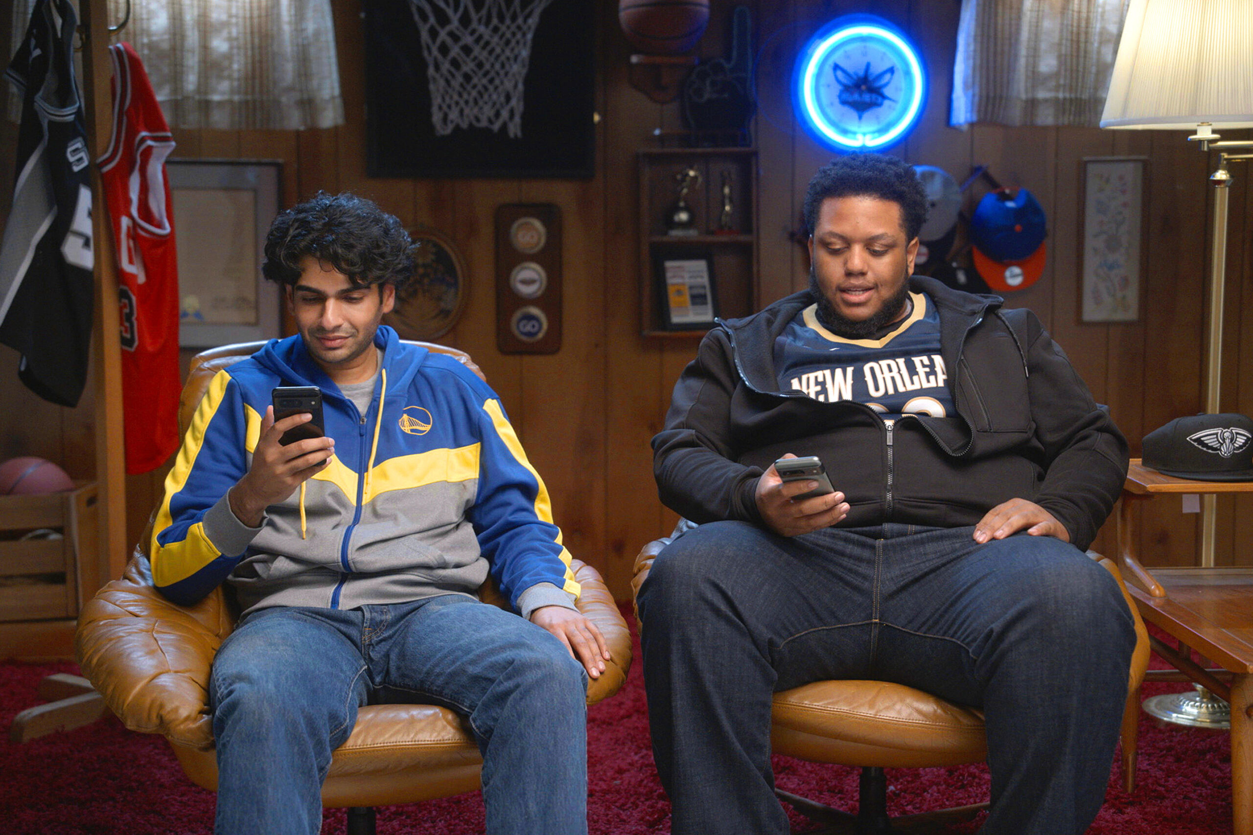 Two men sitting in chairs looking at their phones.