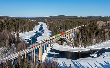 Un trein, yama CargoNet 185, biahando for di ciudad Narvik pa Oslo, capital di Noruega, ta crusa rio Vindelälven entre Vindeln y Tvärålund na Suisia.