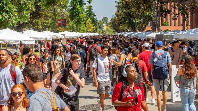 Students walk along the sidewalk and look through booths.