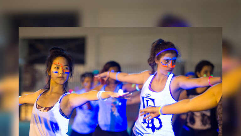 Students in glow paint practicing yoga on the lawn at night.