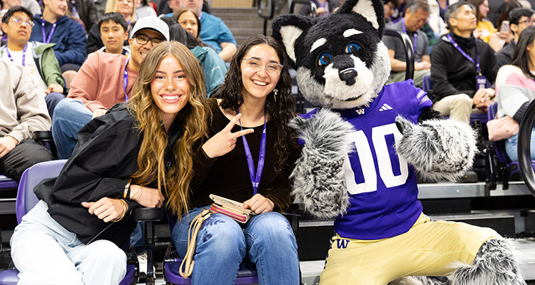 Harry Husky poses for a photo with two people at in the stands at Alaska Airlines Arena.