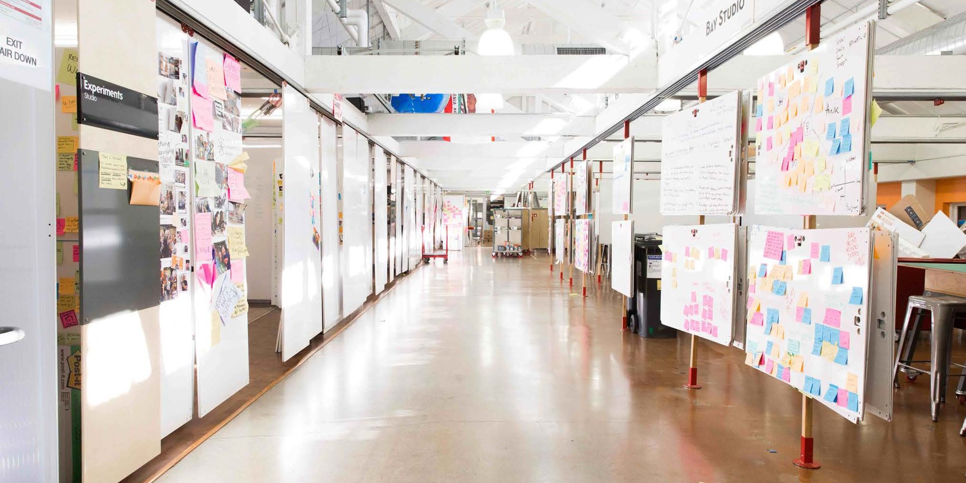 Image of interior of Bay Studio at Stanford's d.school. Halls are lined with posters covered in colorful post it notes.