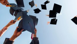 Cropped Hands Of People Throwing Mortarboards Against Clear Sky