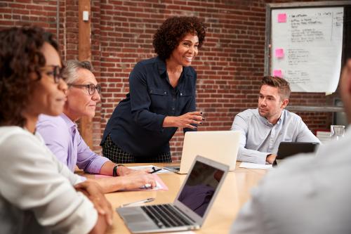 Mature Businesswoman Standing And Leading Office Meeting Around Table