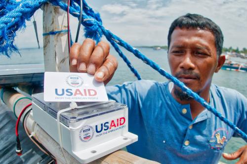 A fisherman holds up a card with the USAID seal on it, attached to a device on his boat