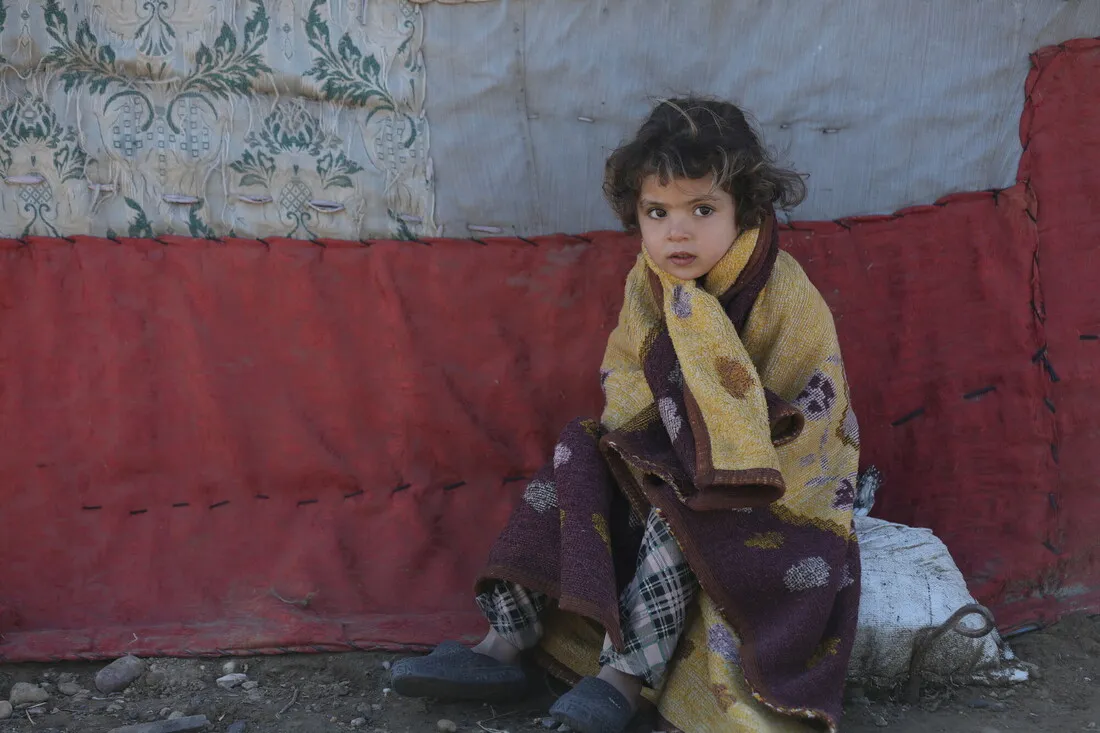 A young girl huddles outside a tent in a fleece blanket.