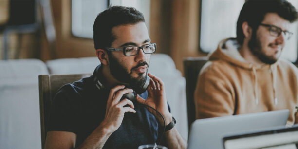 Man in black tshirt sititng at desk with headphones resting around his neck