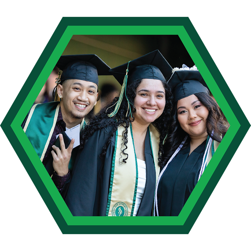 Three students with graduation gowns smiling to the camera.