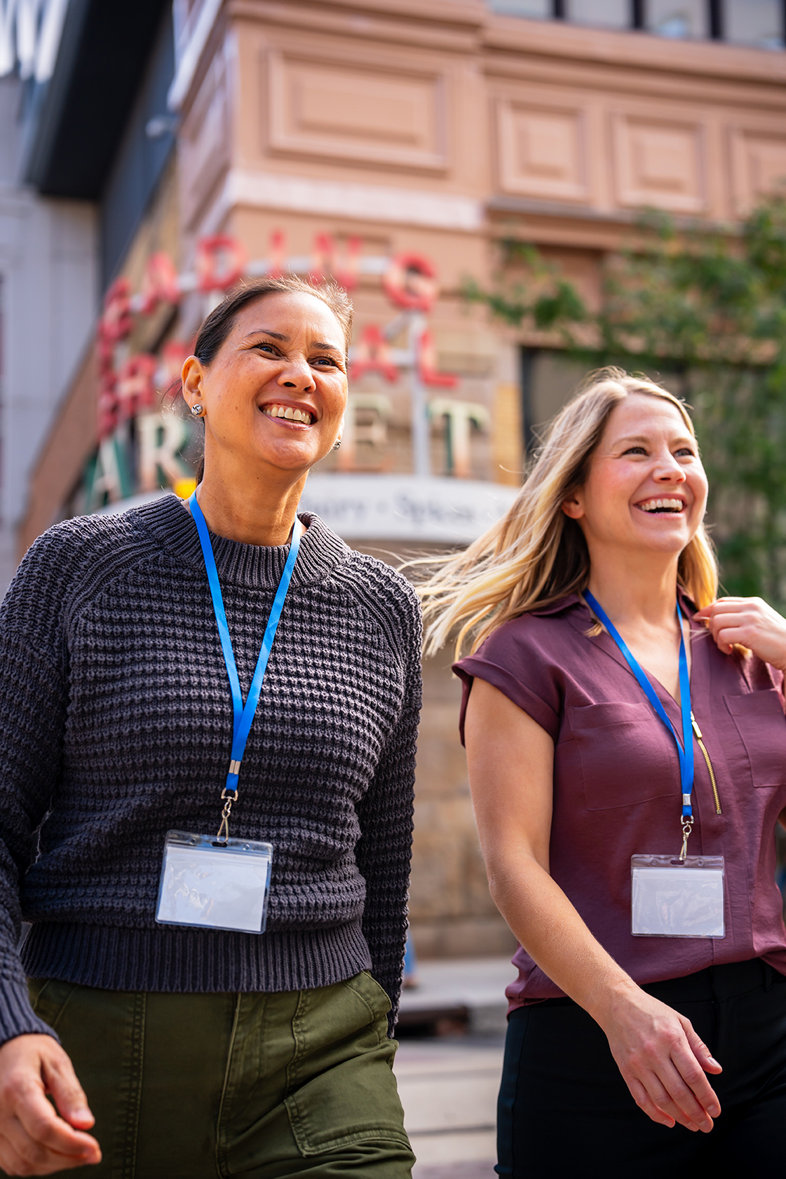 Two people with convention badges laugh while walking down the street.