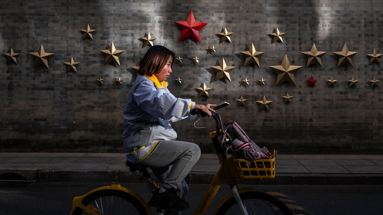 A woman rides a bike by a wall of a historic building adorned with a red star in an upscale commercial area in Beijing, China.